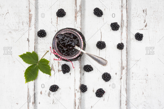 Glass of homemade blackberry jam- blackberries and leaf on wood