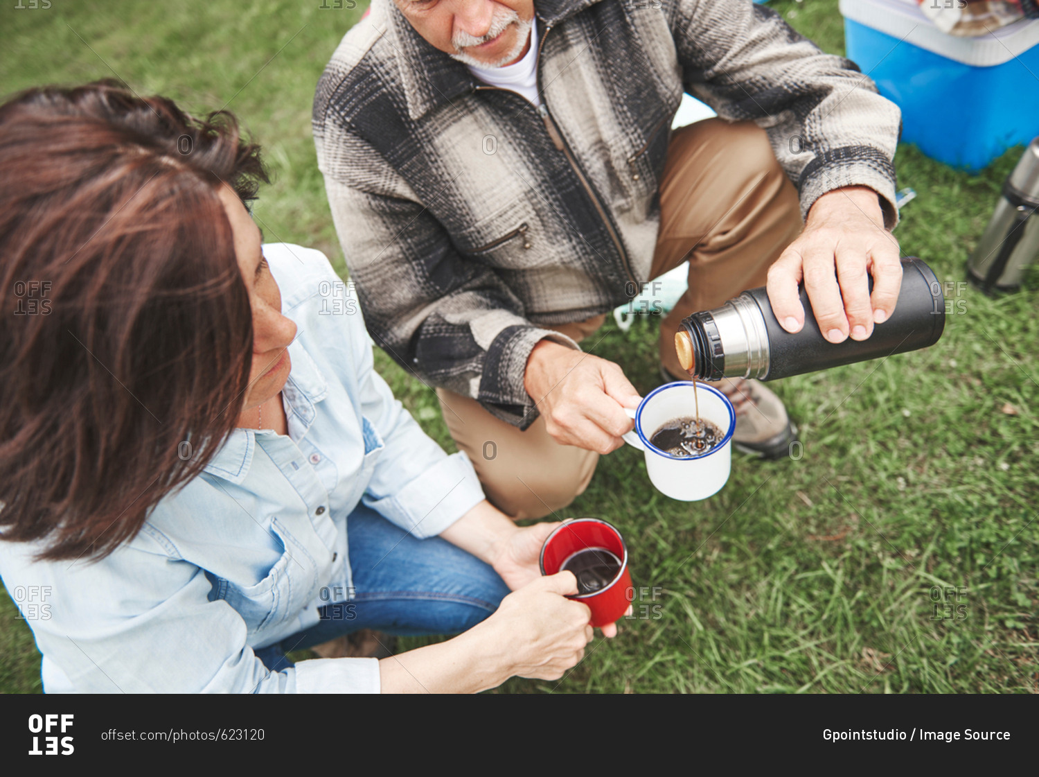 Mature couple crouching on grass, man pouring hot drink from drinks flask, elevated view