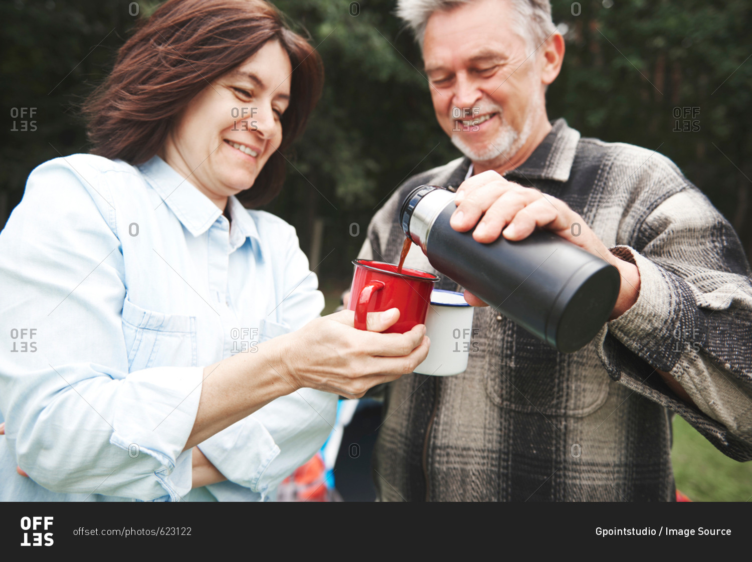 Mature couple outdoors, man pouring hot drink from drinks flask