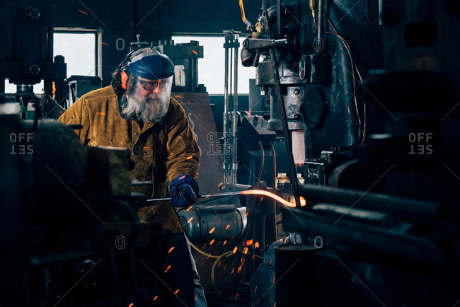 Blacksmith shaping red hot metal rod in workshop