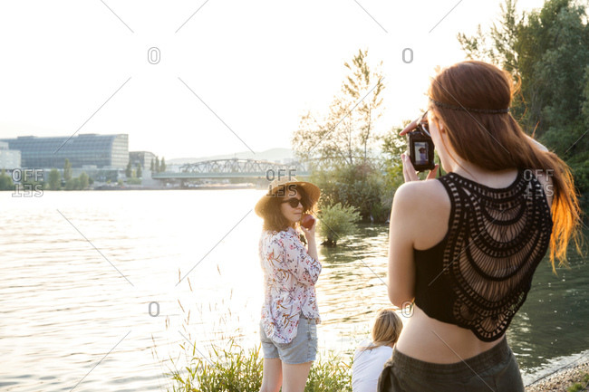 Three female friends at water's edge, young woman photographing friends
