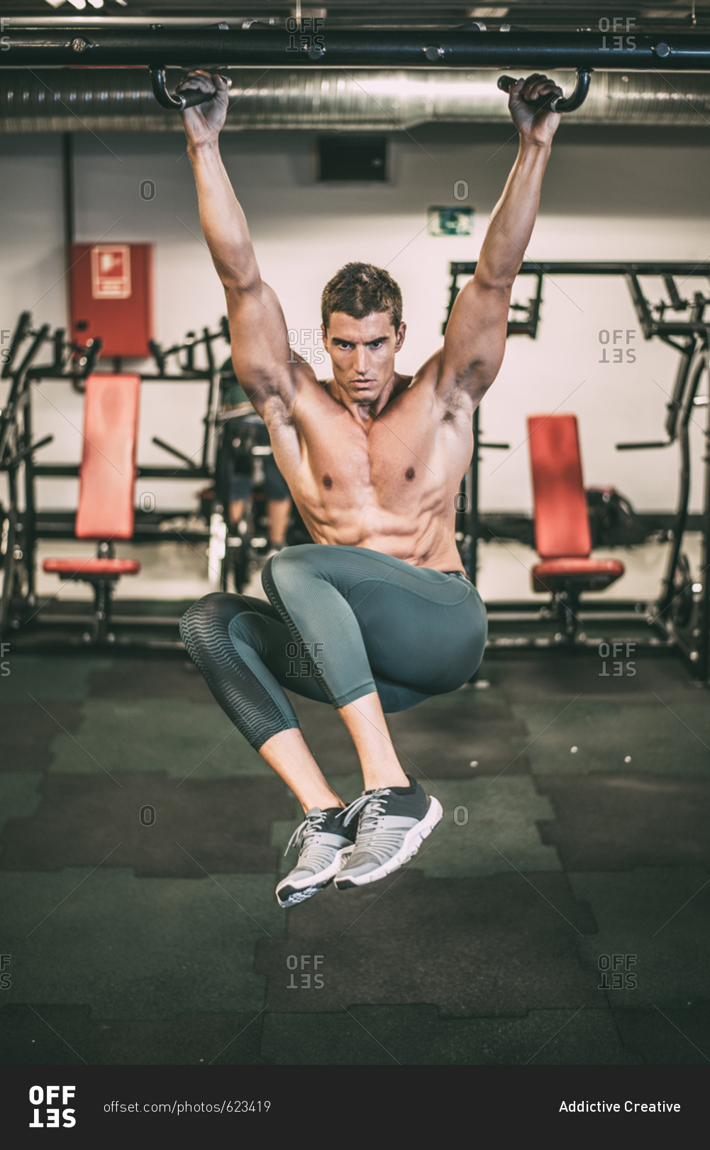 Athletic muscular man hanging and doing chin-ups exercise in gym