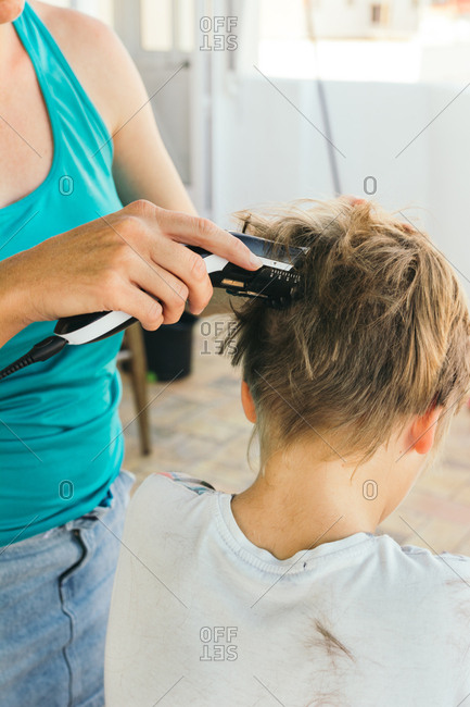 Mother cutting her son's hair, with electric cutting machine, on the terrace of the house