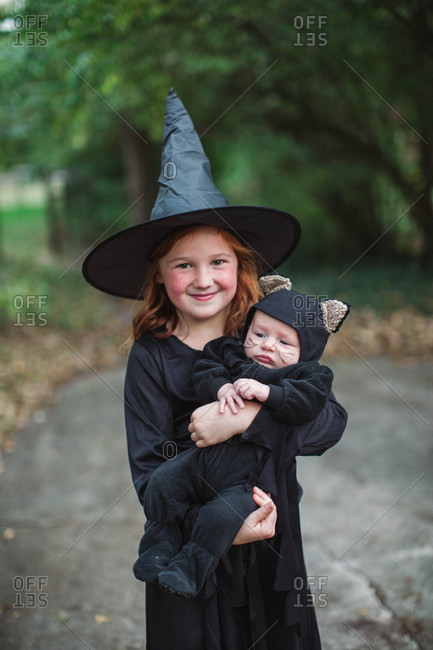 Girl dressed in a witch Halloween costume holding baby dressed as a black  cat stock photo - OFFSET