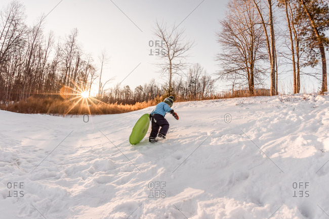 Young boy hauling a sled to the top of a hill
