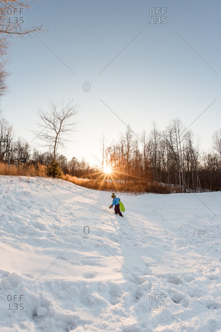 Young boy climbing a snow covered hill with a sled