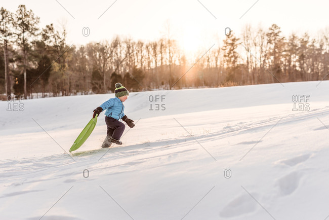 Young boy running up a hill with a sled