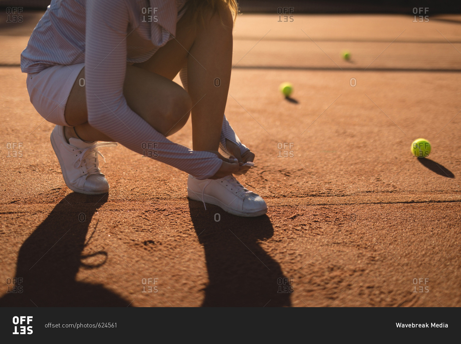 Tennis player tying shoelace in ground on a sunny day