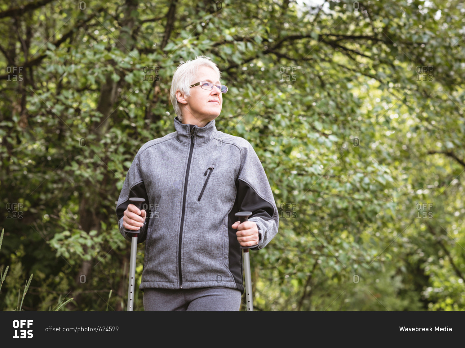 Senior woman hiker walking with hiking poles in the forest