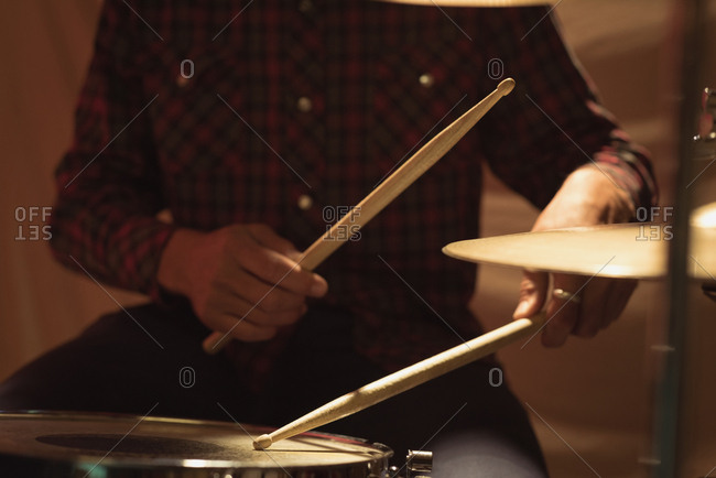 Mid section of drummer playing on drum set at studio