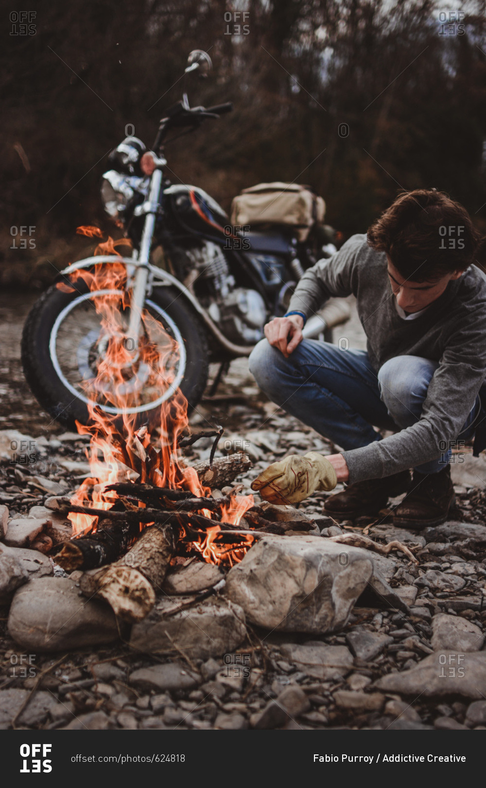 Man keeping campfire burning adding woods on background of parked