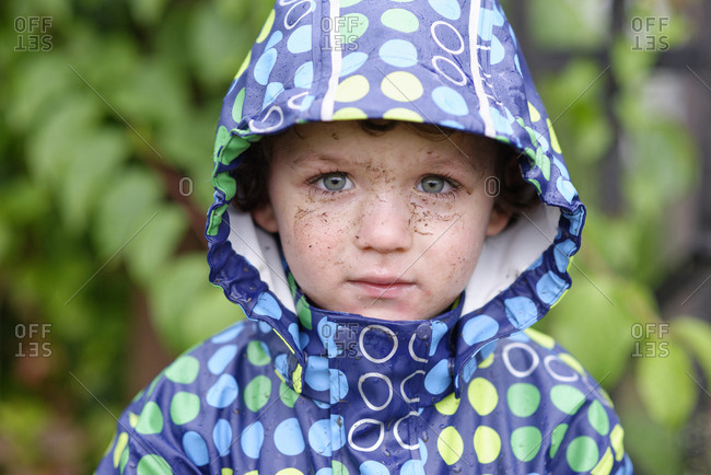 Portrait of little boy with dirty face wearing hooded jacket in rain