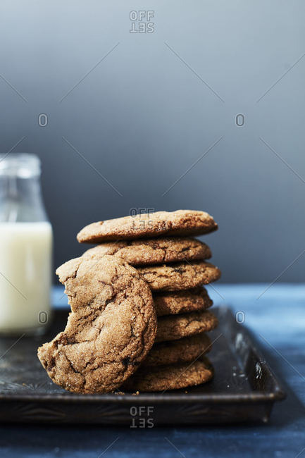 Stack of cookies and one missing a bite on a tray with milk in background