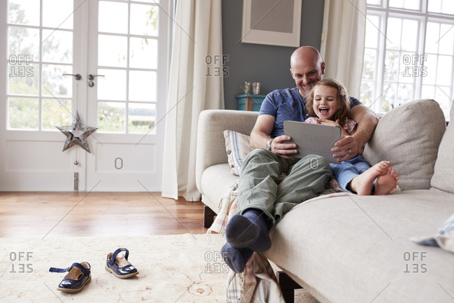 Dad and daughter on couch at home using a tablet computer