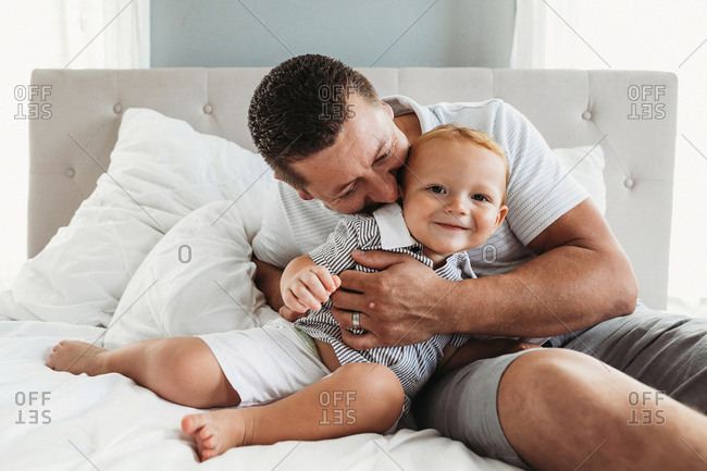 Father and son smile together while cuddling and playing in bed