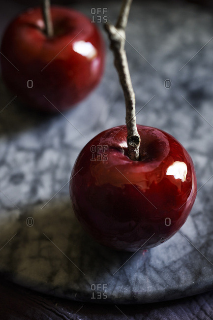 Detail shot of shiny, red, candy apple with twig stick on a marble tray. Moody, dark feel.