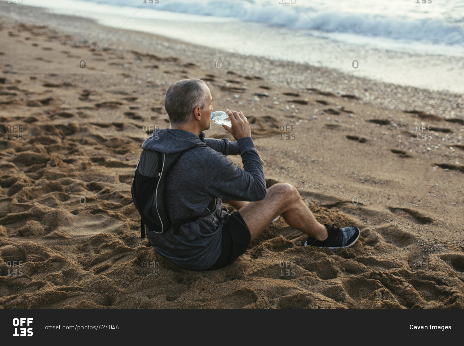 High angle view of man drinking water while sitting at beach