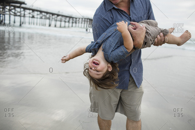 Midsection of playful father carrying son while playing on shore at beach