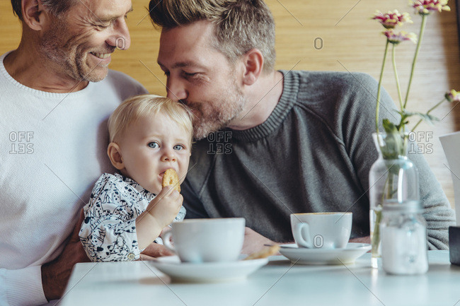 Gay couple cuddling with their baby in cafe
