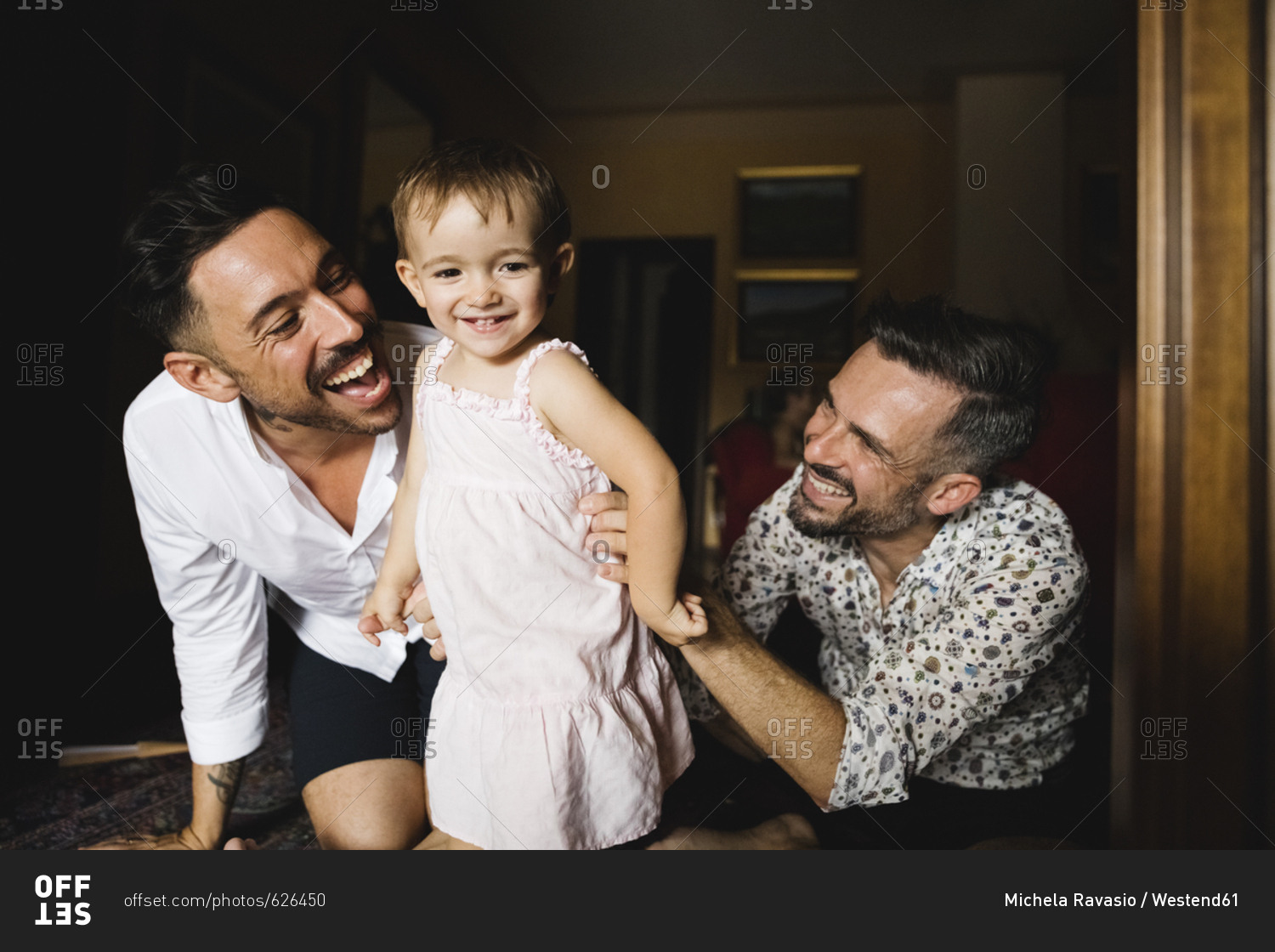 Happy gay couple playing with their little daughter at home