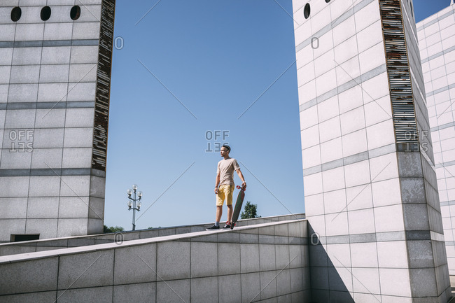 Young man with longboard surrounded by modern architecture