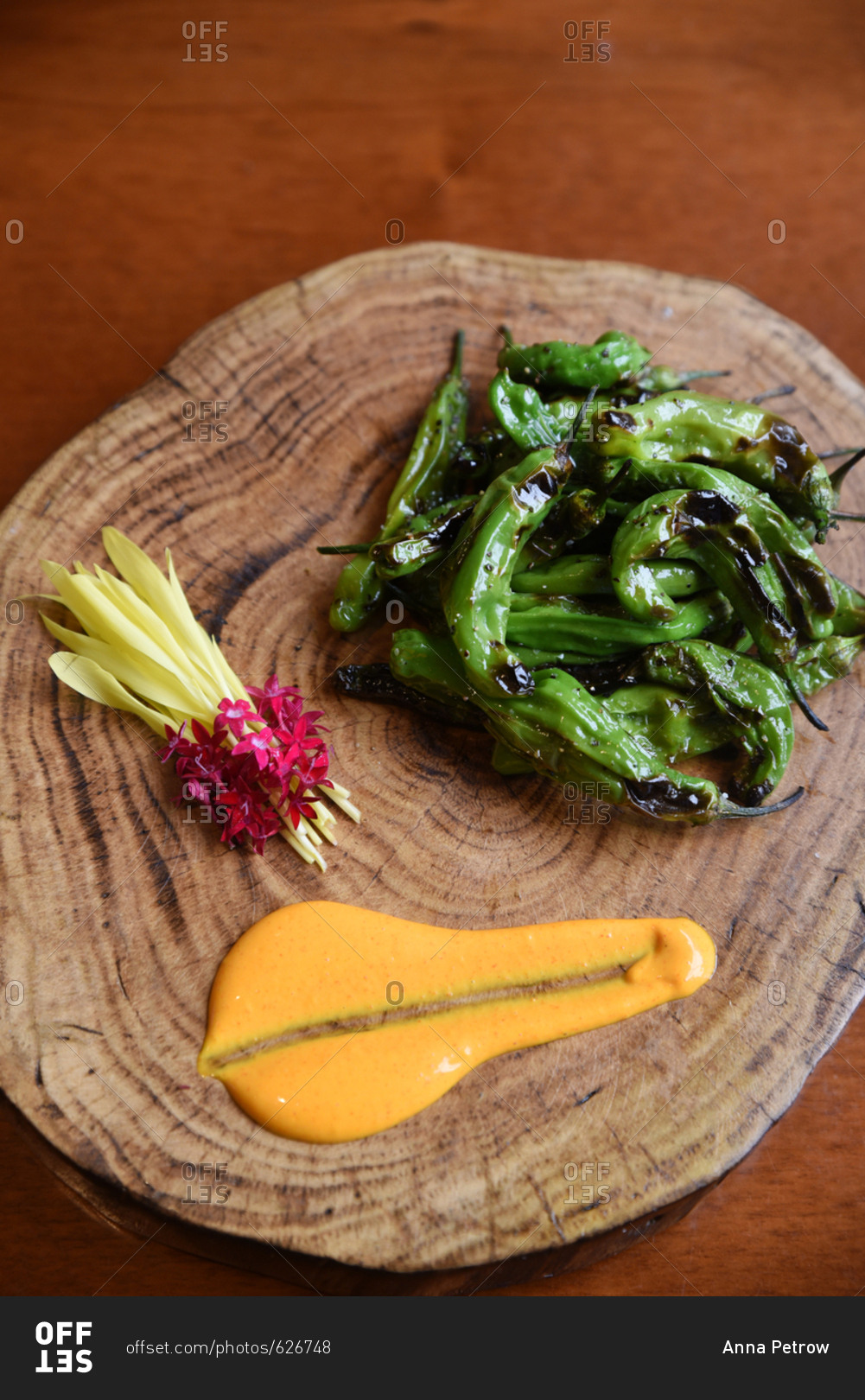 Roasted green chiles on a wooden disk with orange sauce