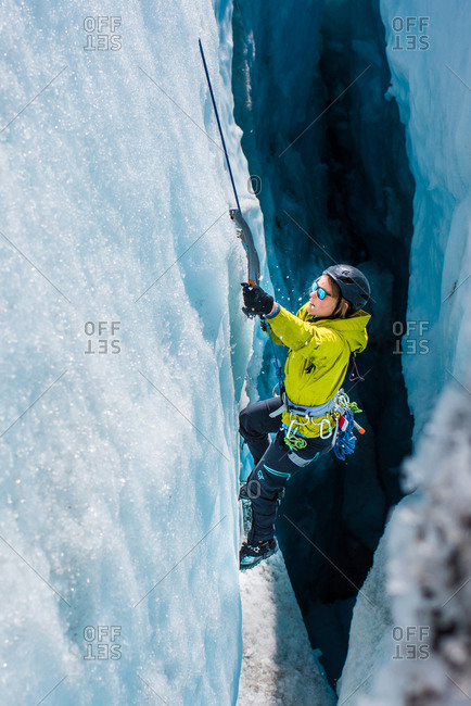 A woman in yellow jacket and sunglasses ice climbing up through a crevasse inside a glacier