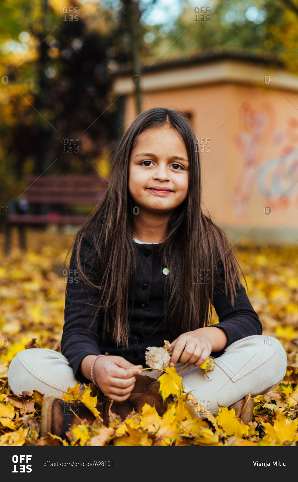 Cute eight year old girl sitting on the ground on a pile of yellow autumn leaves smiling