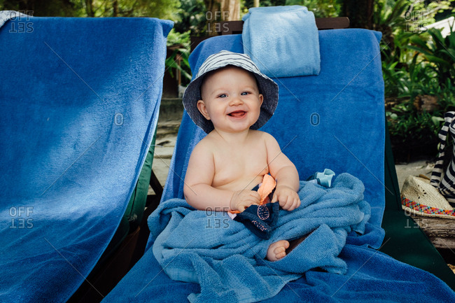 Happy baby sitting on lounge chair with blue towel