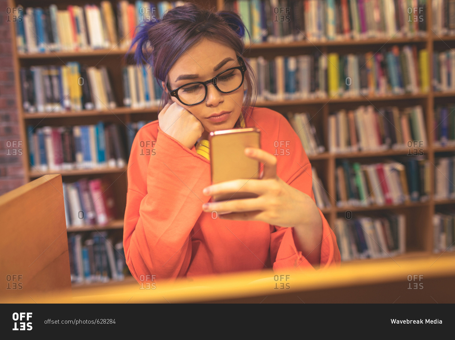 Girl using mobile phone while reading book at desk