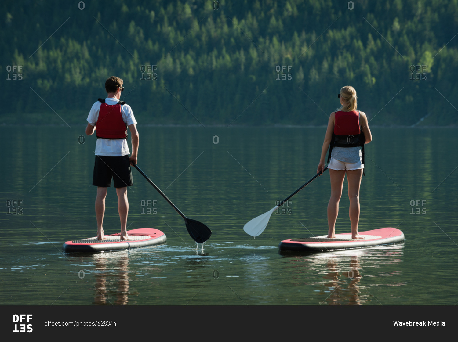 Couple doing stand up paddle boarding in river stock photo OFFSET