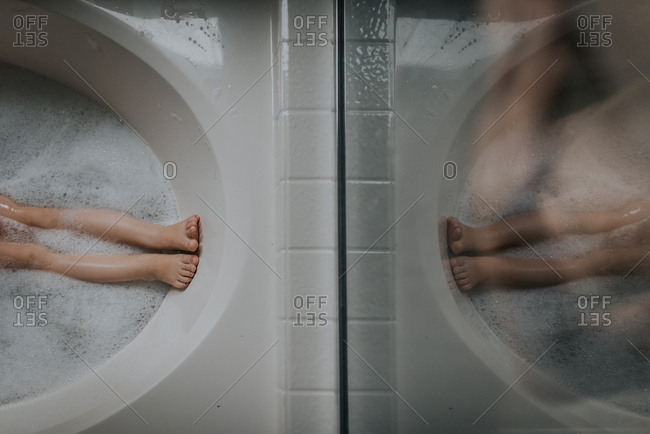 Childs legs reflecting on glass in bathtub
