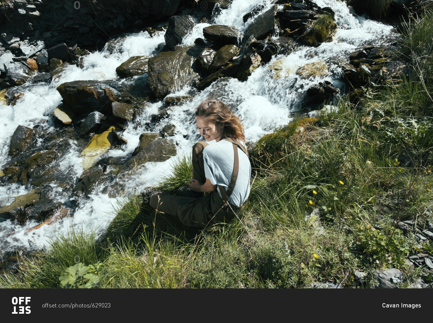 High angle view of cheerful woman looking away while sitting by stream during sunny day