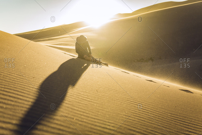 Woman sitting on sand dune at national park during sunset