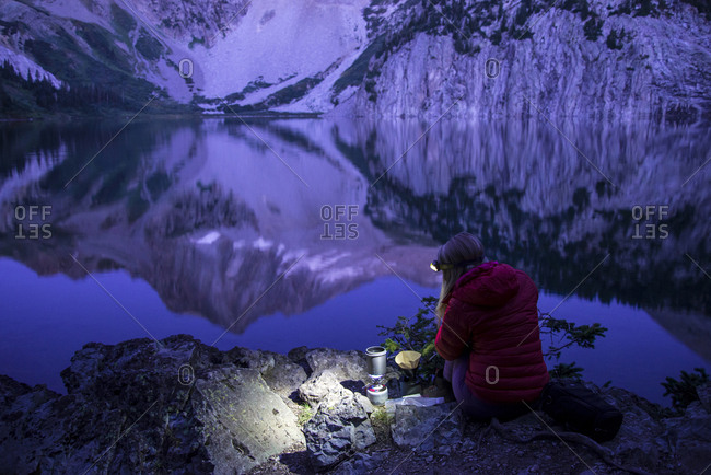 High angle view of female hiker using headlamp while making coffee by lake against mountains
