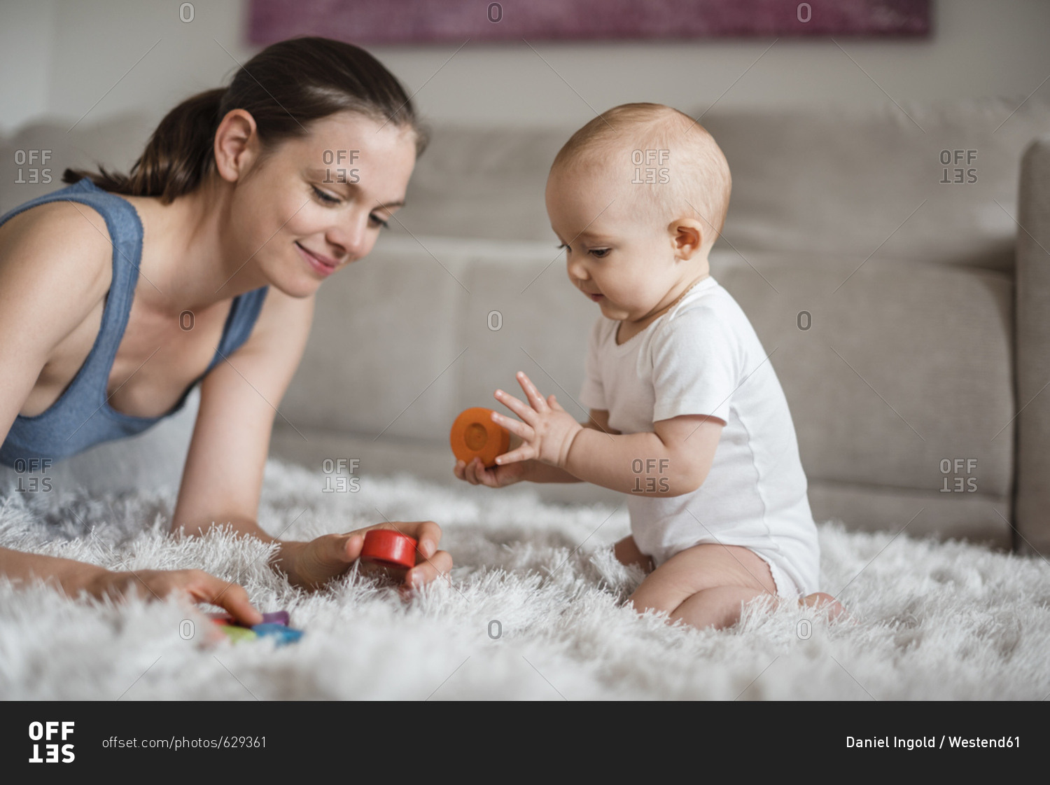 Happy baby girl with mother playing on carpet at home