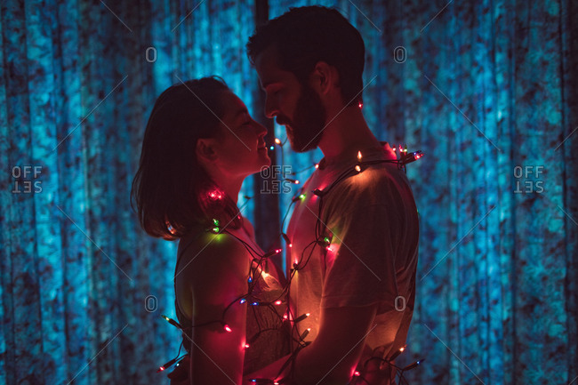 Romantic couple wrapped in fairy lights embracing each other at home