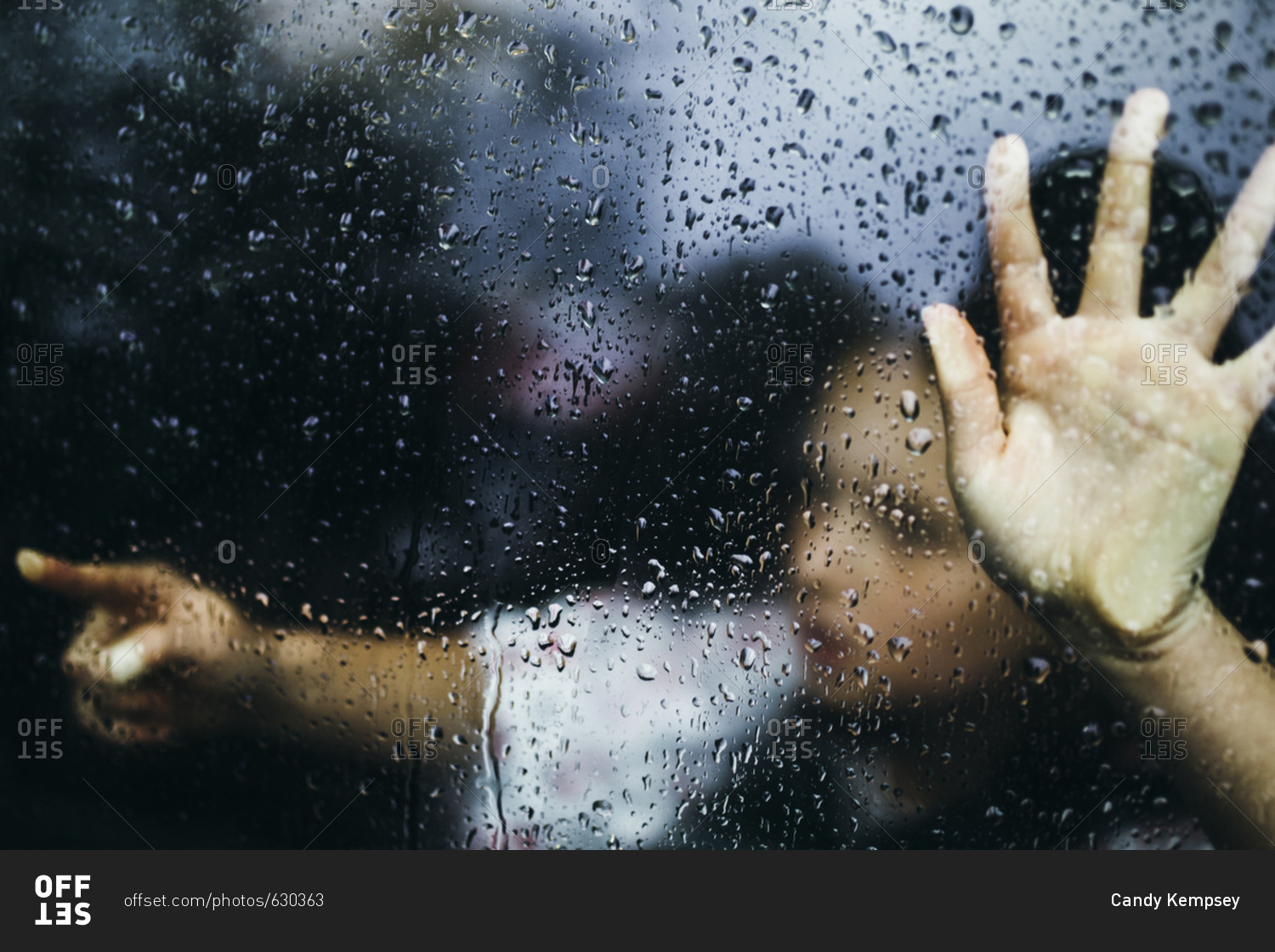 Little girl pointing behind rain covered window