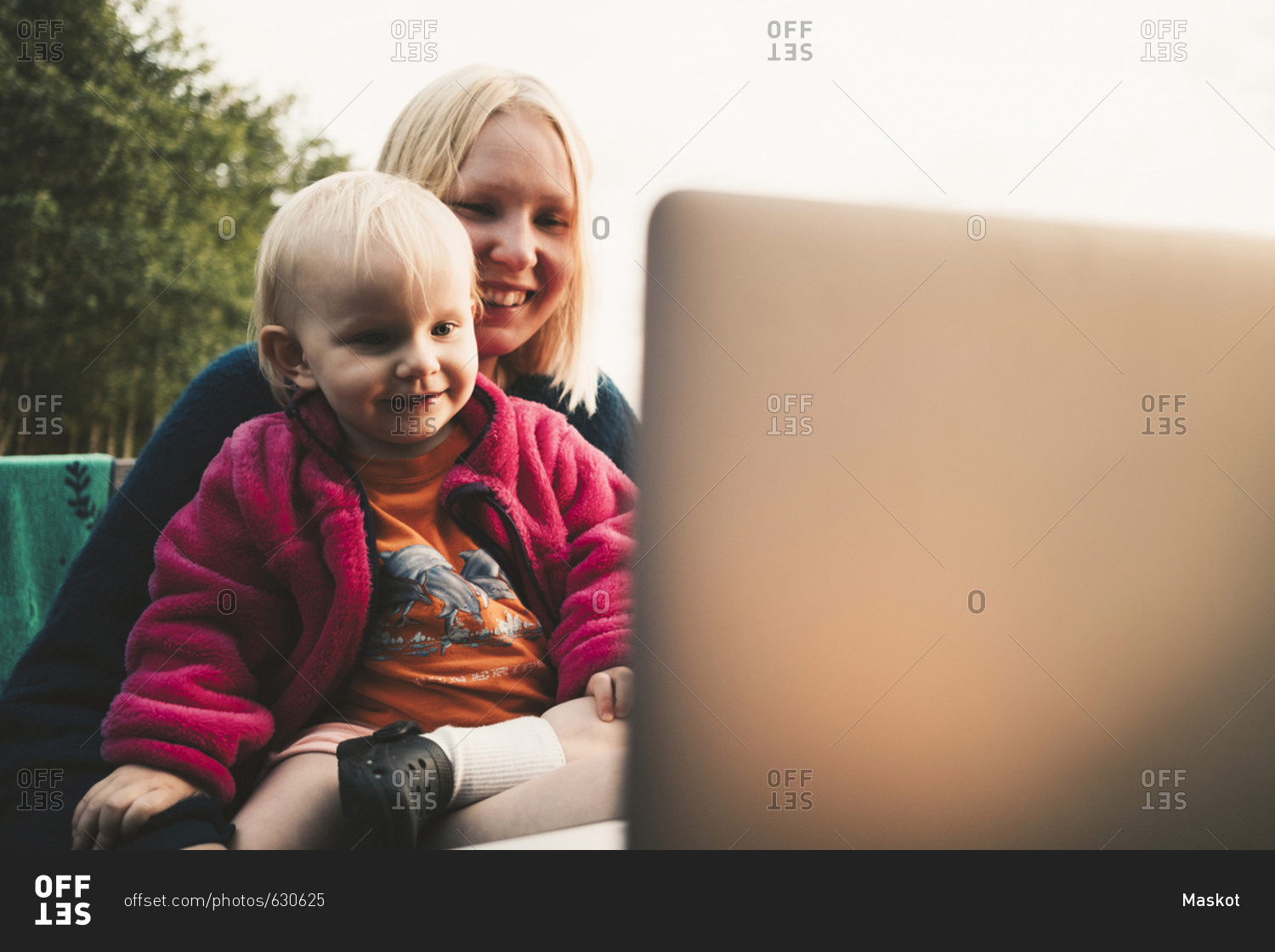 Smiling mother and daughter looking at laptop during video conference on sunny day