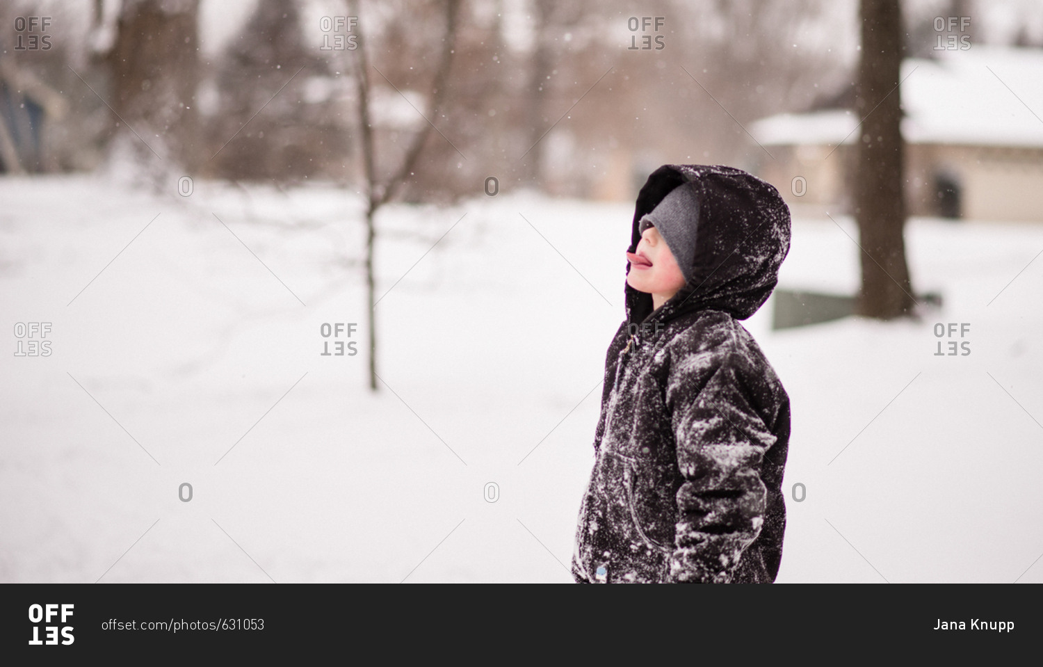 Boy in winter coat covered with snow catching snowflakes on his tongue