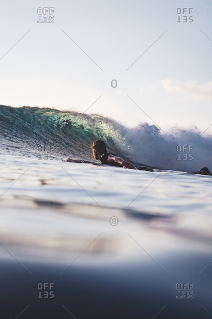 Person paddling on surfboard into rolling wave