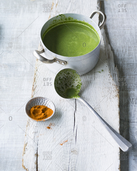Pot of spinach soup and soup ladle on wood