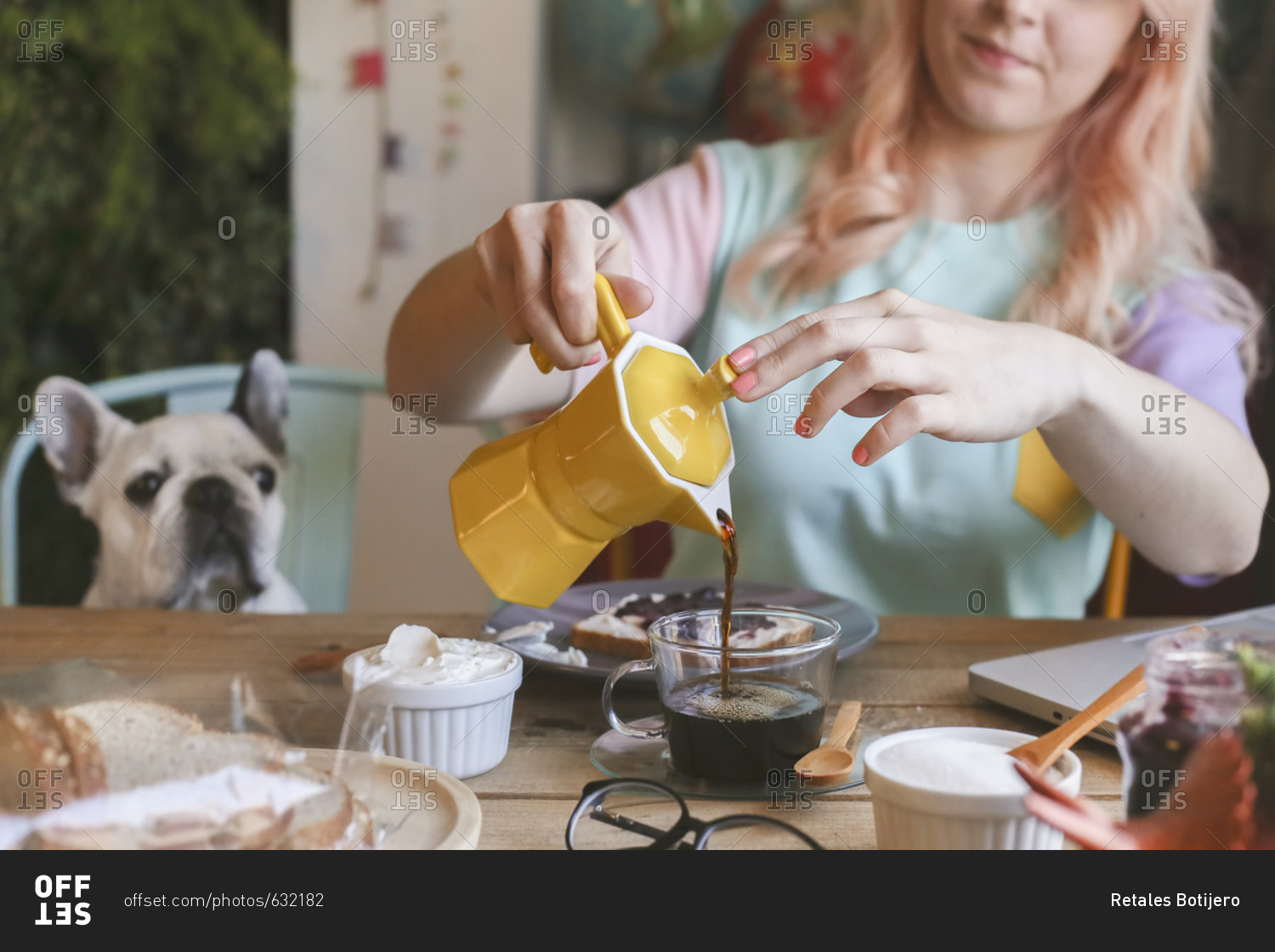 Young woman having breakfast and using laptop at home with her dog