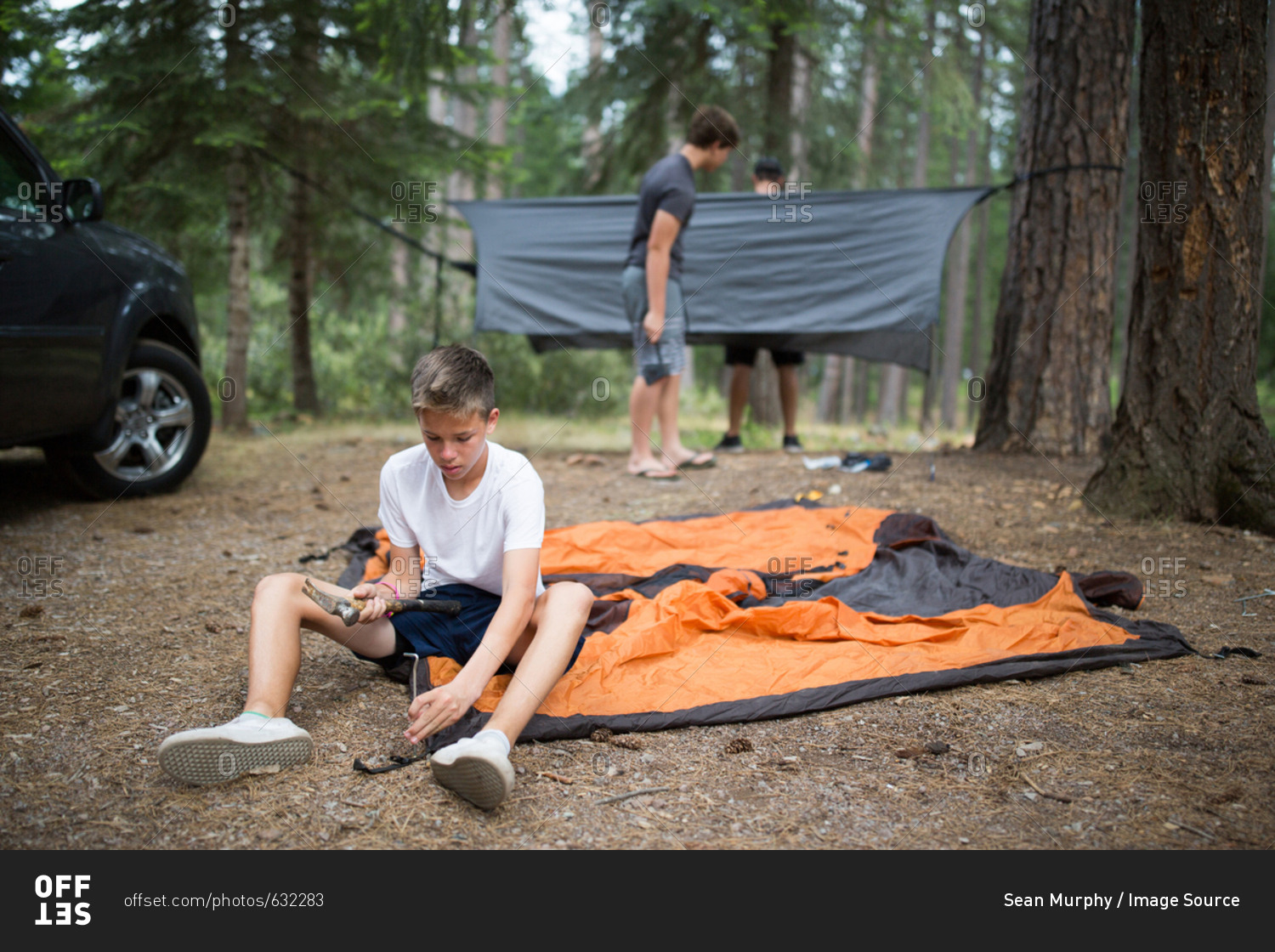 Teenage boy hammering in tent peg, friends in background