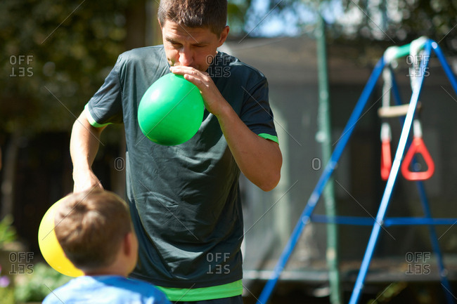 Father and son in garden, father blowing up balloons