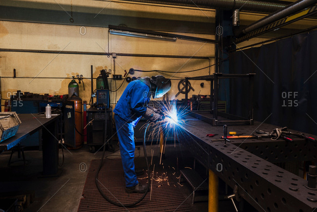 Man in welding mask cutting steel in factory