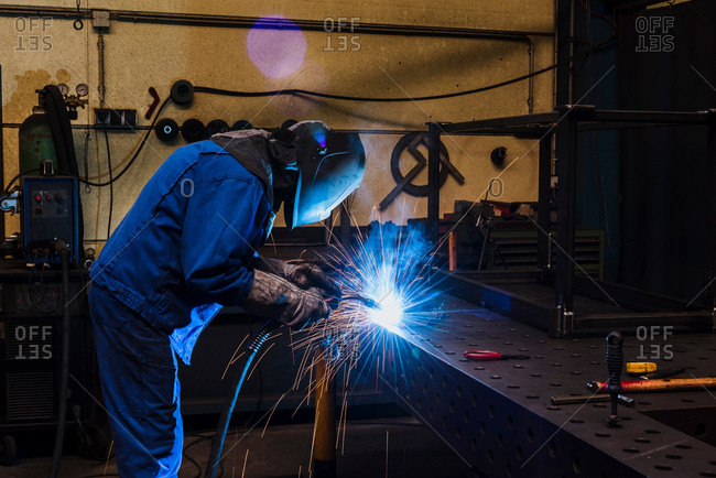 Man in welding mask cutting steel in factory