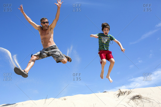 A Man And Boy Jumping On Sand Dune In Provincetown