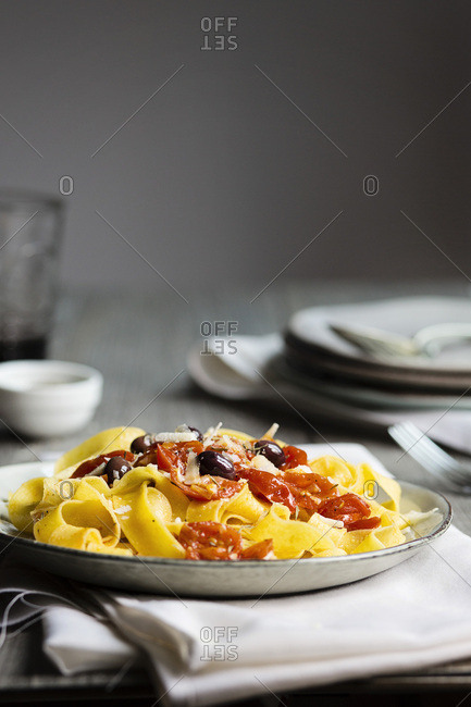 A typical italian dish pappardelle pasta with tomato sauce, olives and parmesan on wooden table
