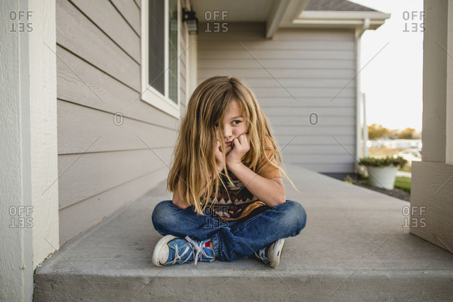 Little boy with long hair pouting on a porch stock photo - OFFSET